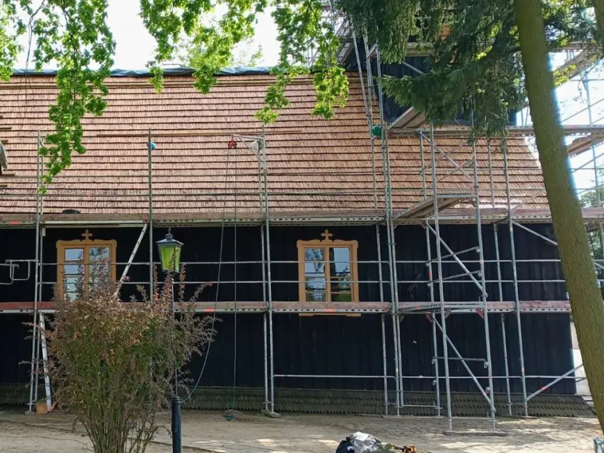 Dom z dachem z gontu drewnianego podczas prac przy elewacji, widoczne rusztowania